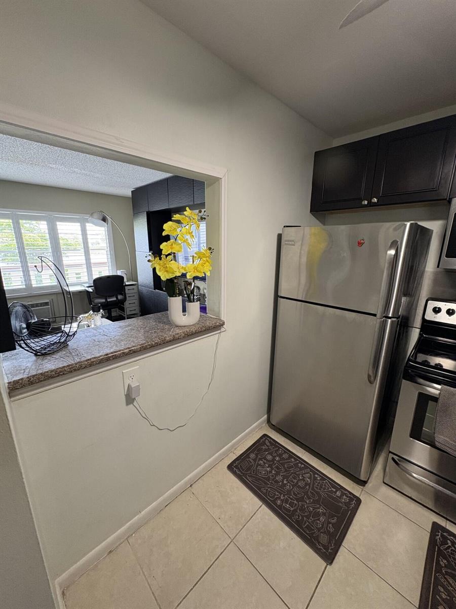 A kitchen with stainless steel appliances, dark cabinets, and a pass-through window to another room — 65 Preston B, Boca Raton FL 33434, BOCA RATON, FL