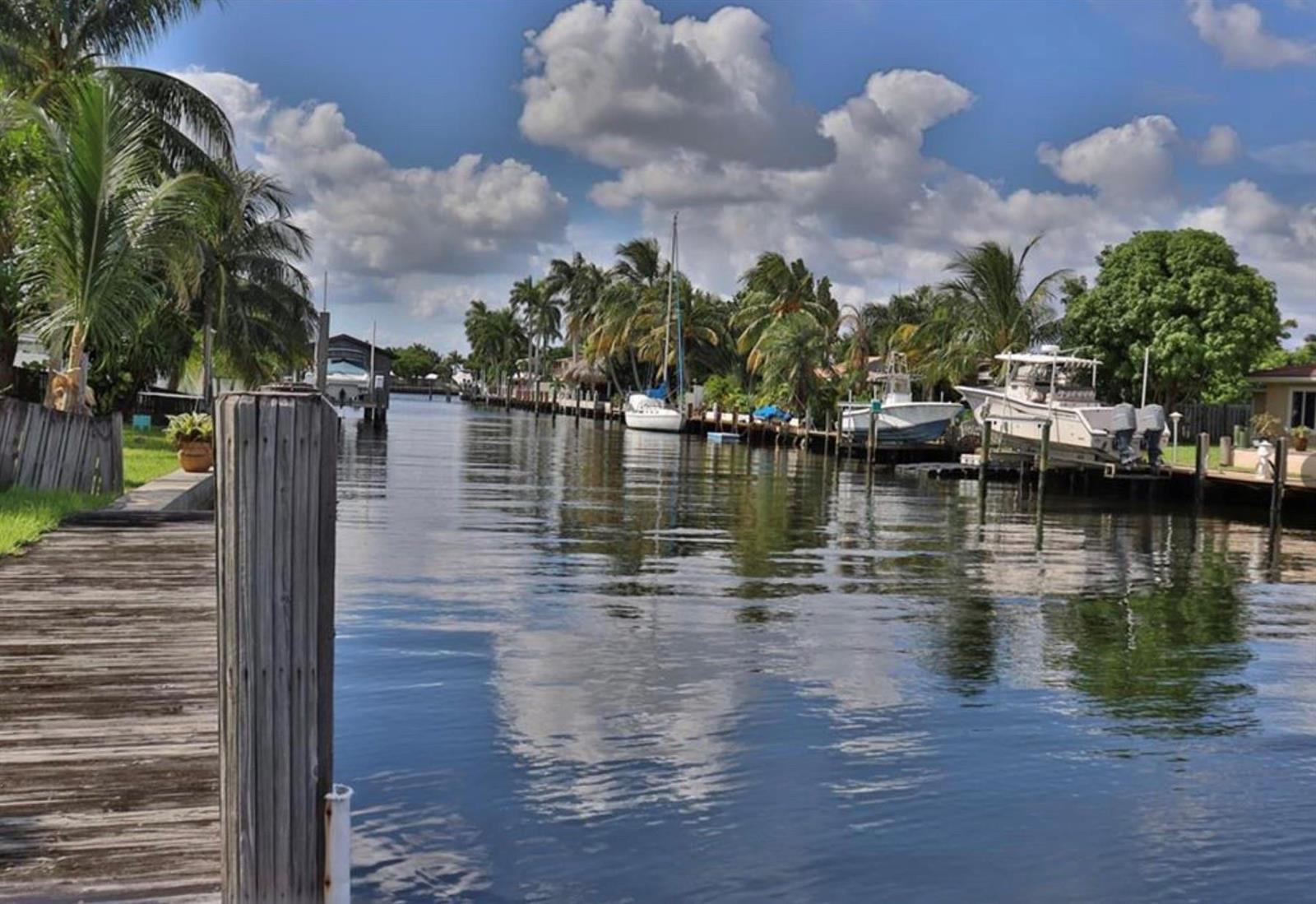 A wooden dock overlooks a canal lined with palm trees and several docked boats — 5 Sunset Lane, Pompano Beach FL 33062, POMPANO BEACH, FL