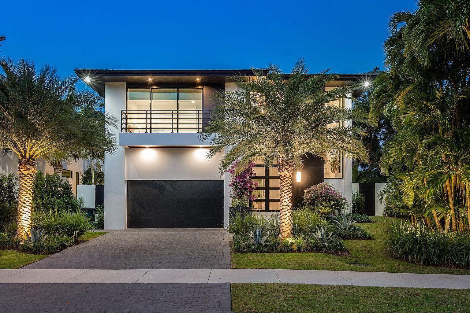 A modern two-story house with a black garage door, balcony, and illuminated palm trees at dusk — 775 W Park Dr Drive W, Boca Raton FL 33432, BOCA RATON, FL