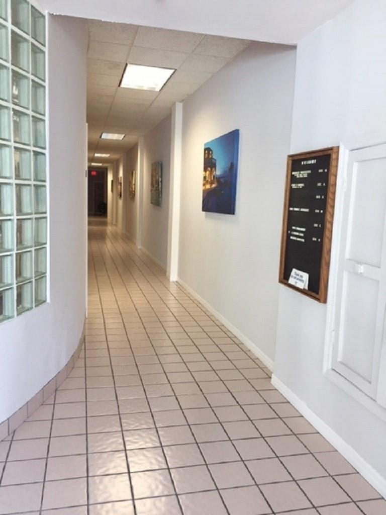 A long hallway features light-colored floor tiles, a glass block wall, and framed wall art — 2012 Hollywood Bl # D, Hollywood FL 33020, HOLLYWOOD, FL
