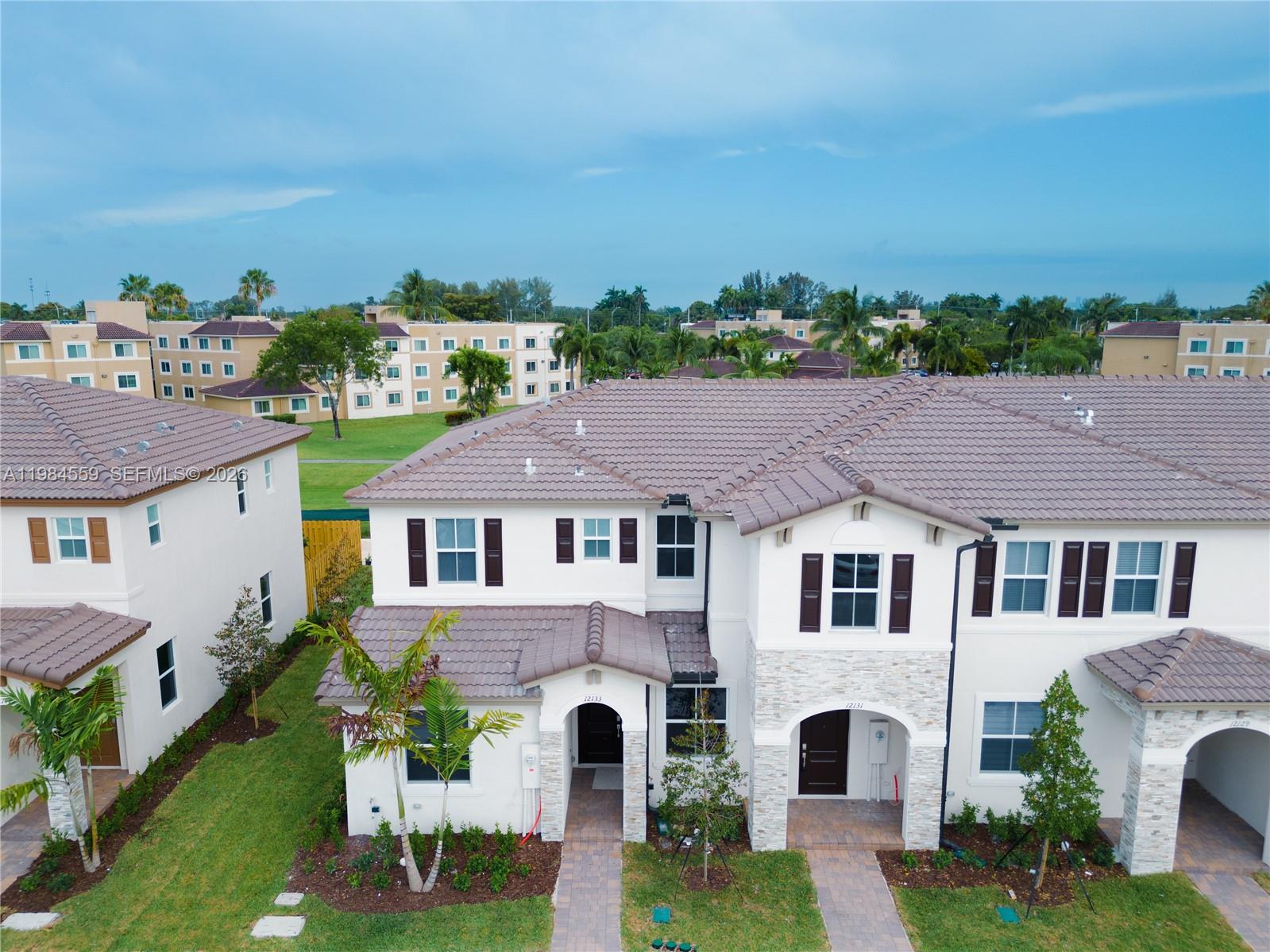 An aerial view shows the exterior of two-story townhouses with tiled roofs and stone accents — 12133 NW 23rd Ct, Miami FL 33167, MIAMI, FL