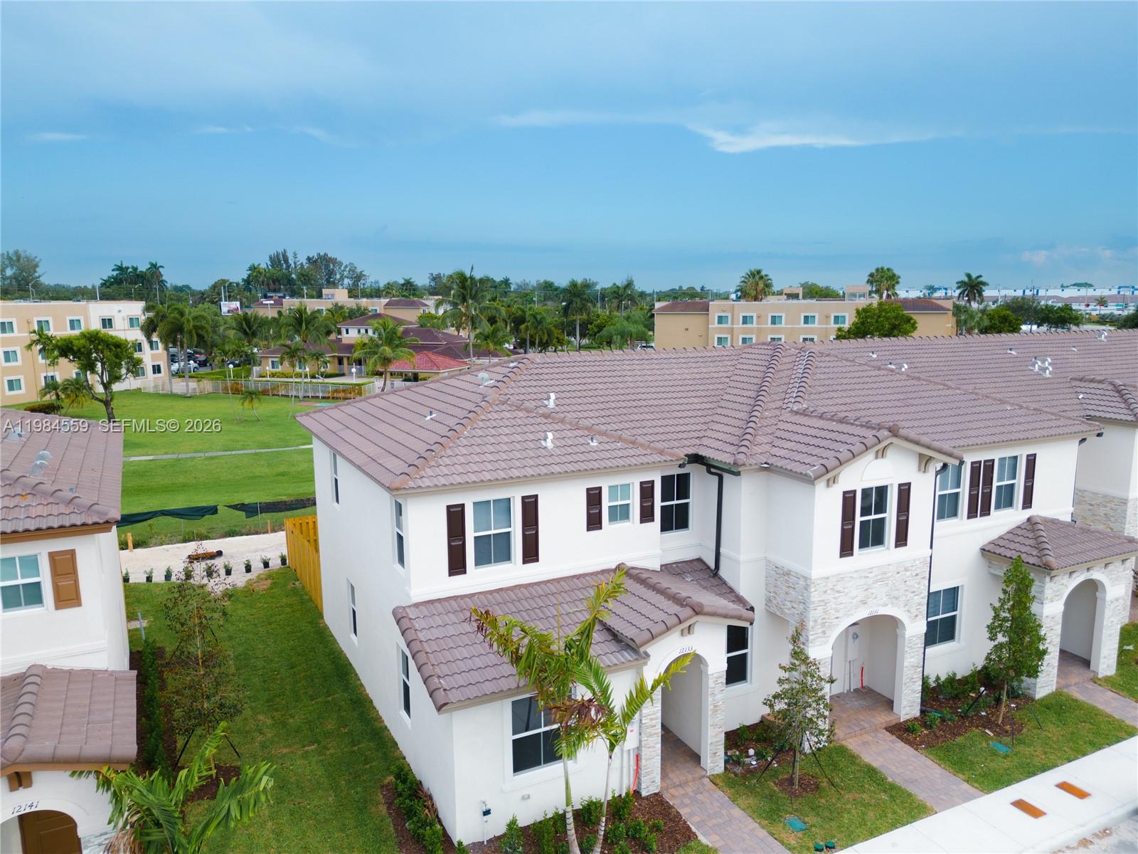 An aerial view shows two-story white stucco townhomes with brown tile roofs and landscaping — 12133 NW 23rd Ct, Miami FL 33167, MIAMI, FL