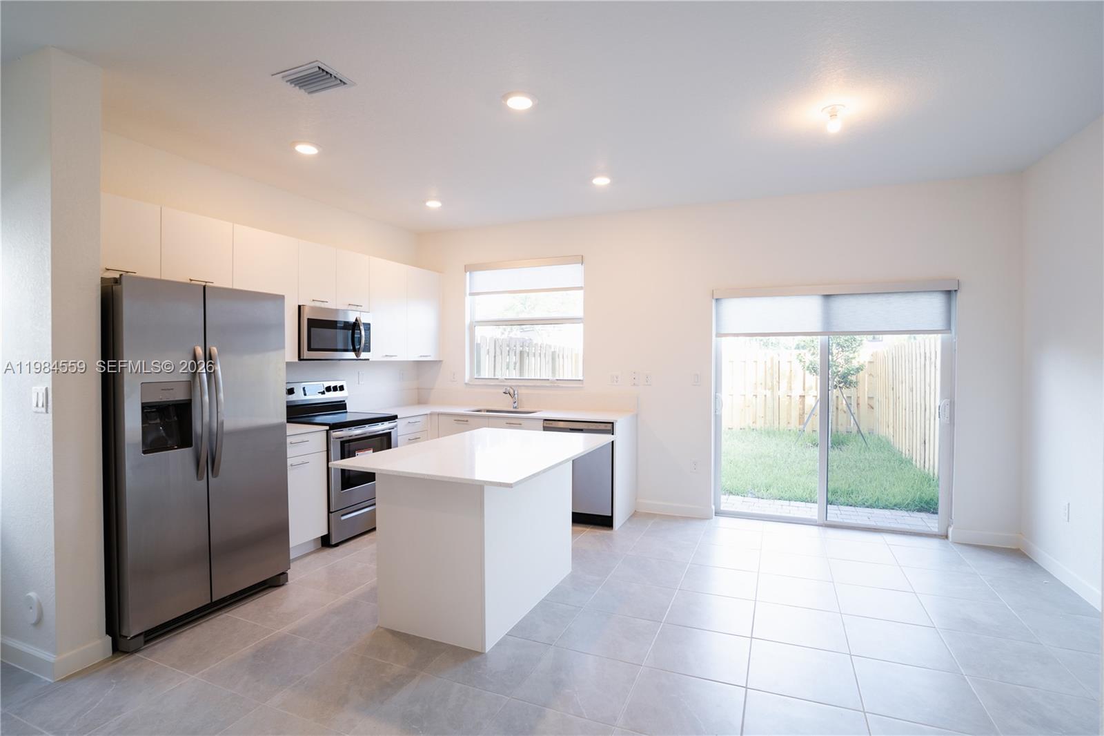 A modern kitchen features white cabinetry, stainless steel appliances, a center island, and tile flooring — 12133 NW 23rd Ct, Miami FL 33167, MIAMI, FL