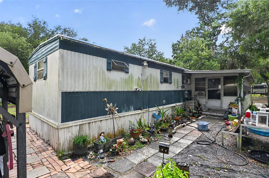The exterior of a weathered mobile home features a patio area with potted plants — 26322 BRAHMA DRIVE, WESLEY CHAPEL, FL