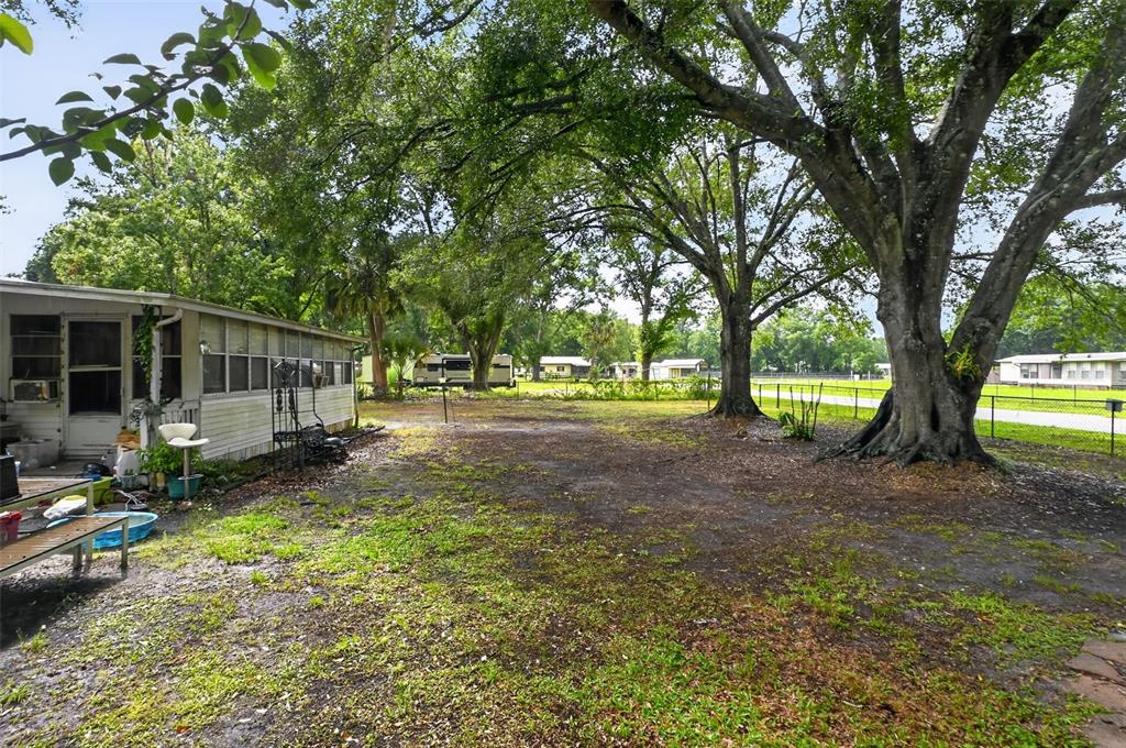 A grassy yard with large trees sits beside a white mobile home — 26322 BRAHMA DRIVE, WESLEY CHAPEL, FL