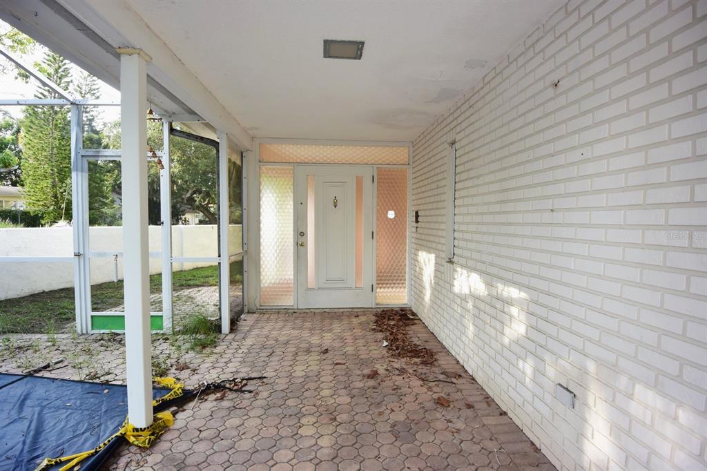 A covered brick patio leads to a white front door with textured glass side panels — 7124 JASMIN DRIVE, NEW PORT RICHEY, FL