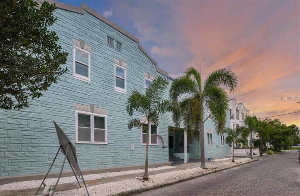 A light blue, multi-story building with textured siding stands along a paved street at sunset — 308 GROVE STREET N UNIT 102, ST PETERSBURG, FL