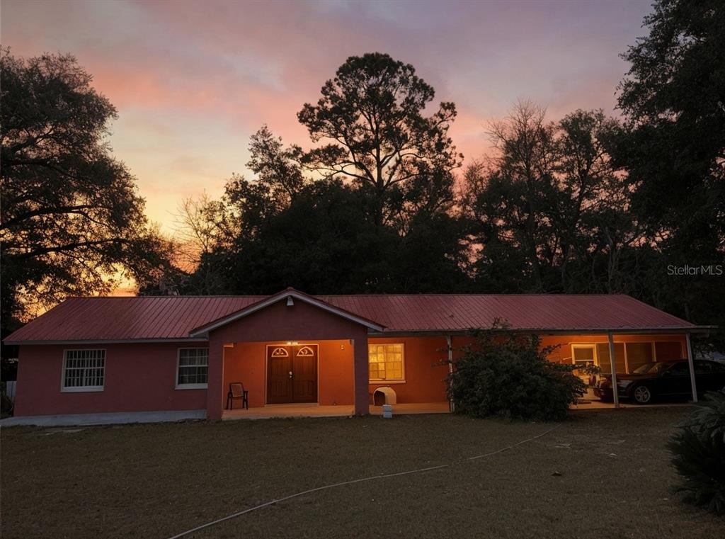 A single-story house with a red metal roof and a covered porch at sunset — 912 NE 144TH COURT, SILVER SPRINGS, FL