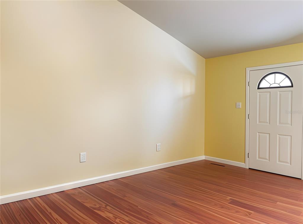 An empty room with yellow walls, hardwood flooring, and a white front door — 912 NE 144TH COURT, SILVER SPRINGS, FL