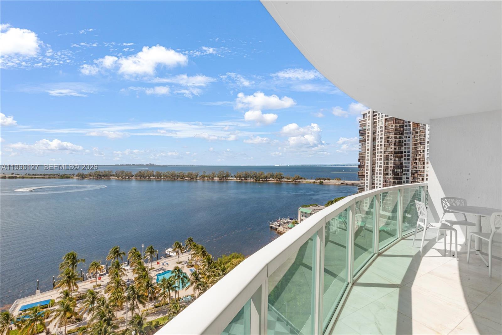 A high-rise balcony overlooks a bay with palm trees, a swimming pool, and distant buildings — 2101 Brickell Ave # 1206, Miami FL 33129, MIAMI, FL