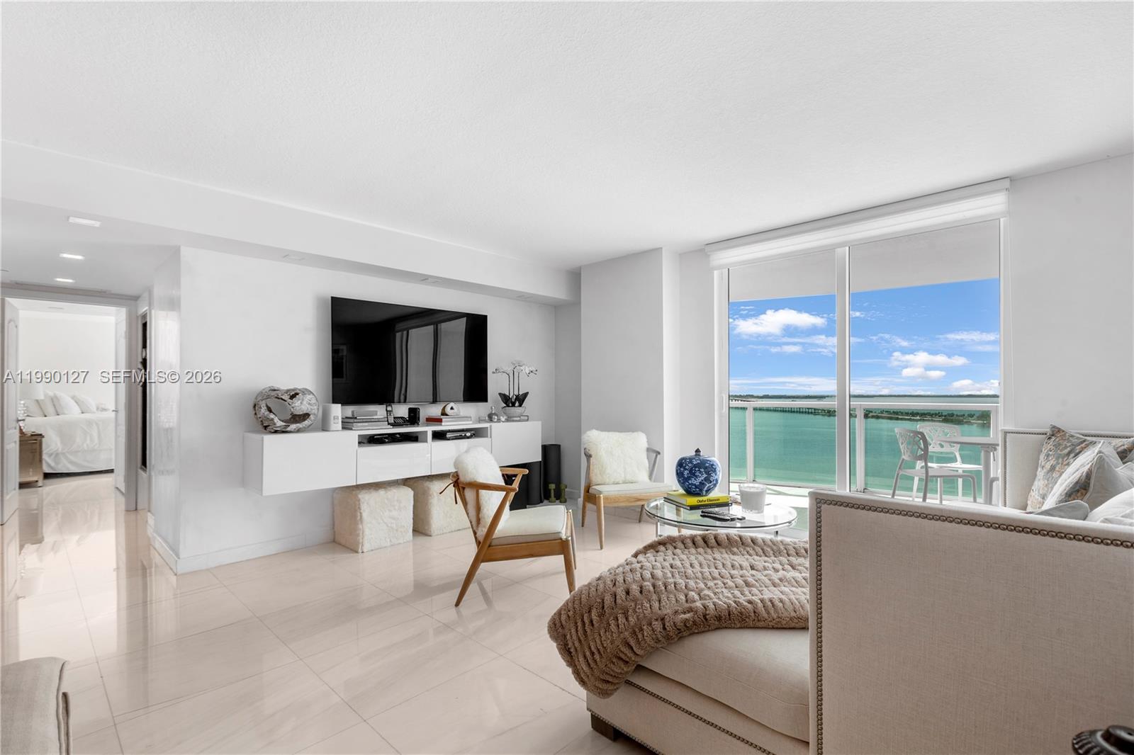 A bright living room features white tile floors, a wall-mounted television, and a balcony view — 2101 Brickell Ave # 1206, Miami FL 33129, MIAMI, FL