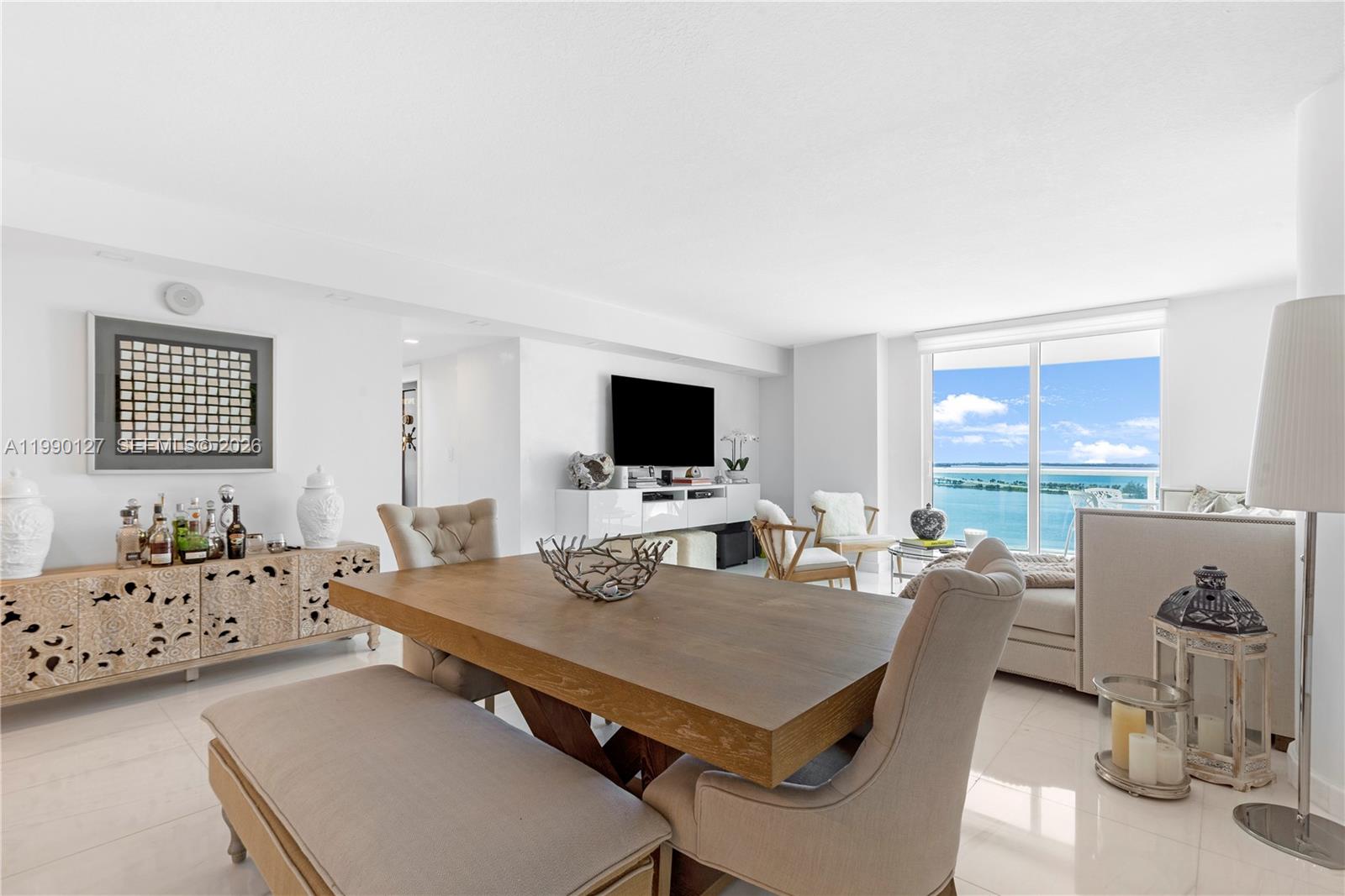 A bright dining and living area features a wooden table, neutral furniture, and ocean views — 2101 Brickell Ave # 1206, Miami FL 33129, MIAMI, FL