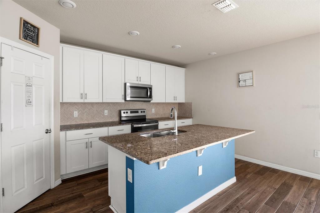 A kitchen features white cabinets, granite countertops, a blue island, and wood-look flooring — 884 CAMBRIDGE DRIVE, WINTER HAVEN, FL