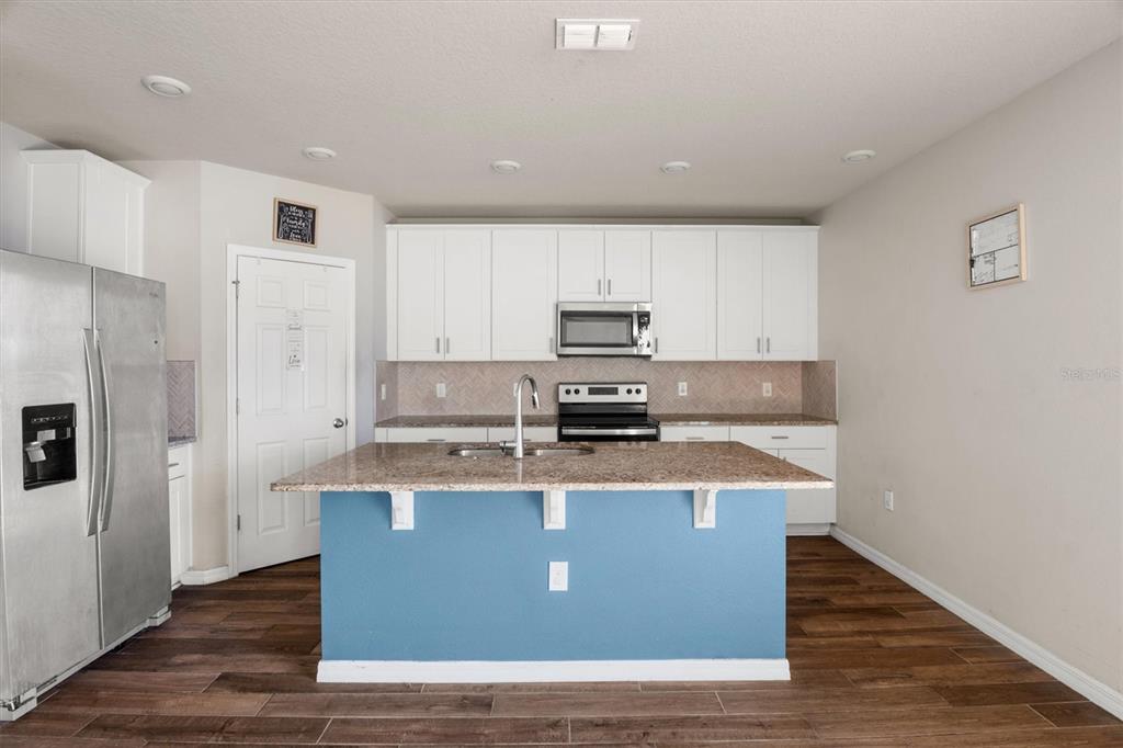 A kitchen features white cabinets, a blue island with a granite countertop, and stainless appliances — 884 CAMBRIDGE DRIVE, WINTER HAVEN, FL