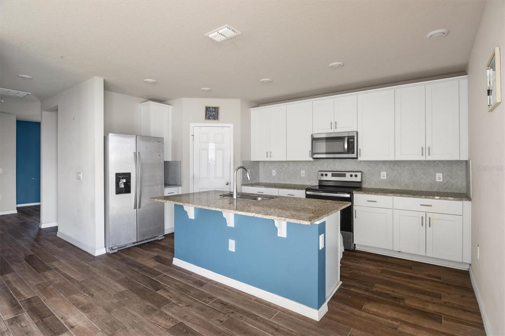 A kitchen features white cabinets, granite countertops, a blue island, and stainless steel appliances — 884 CAMBRIDGE DRIVE, WINTER HAVEN, FL