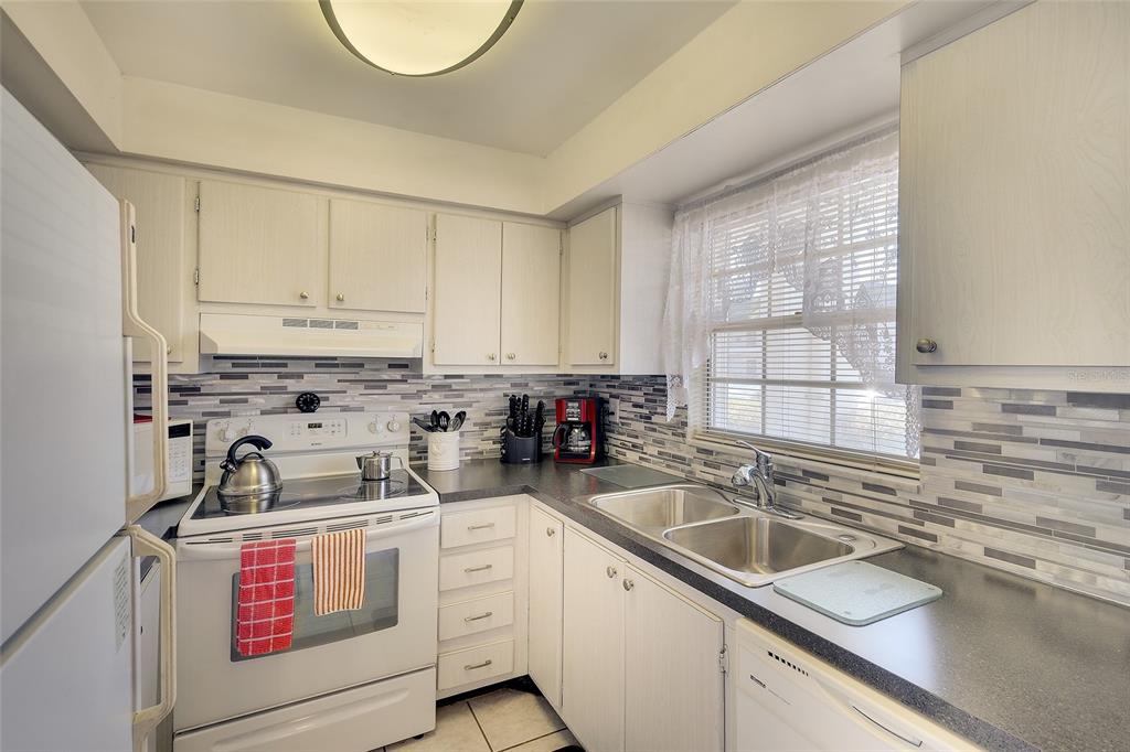 A kitchen with white cabinets, a tiled backsplash, stainless steel sink, and white appliances — 305 47TH AVENUE DRIVE W UNIT 146, BRADENTON, FL