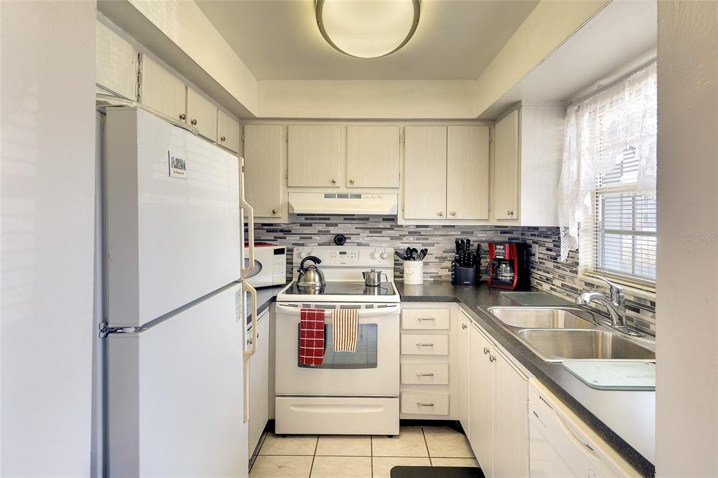 A kitchen features white appliances, light-colored cabinets, a tiled backsplash, and a double-basin sink — 305 47TH AVENUE DRIVE W UNIT 146, BRADENTON, FL