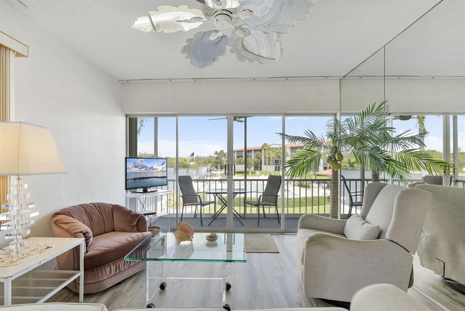 A living room features a glass coffee table, a pink armchair, and sliding doors overlooking water — 101 NE 19th Avenue # 228, Deerfield Beach FL 33441, DEERFIELD BEACH, FL