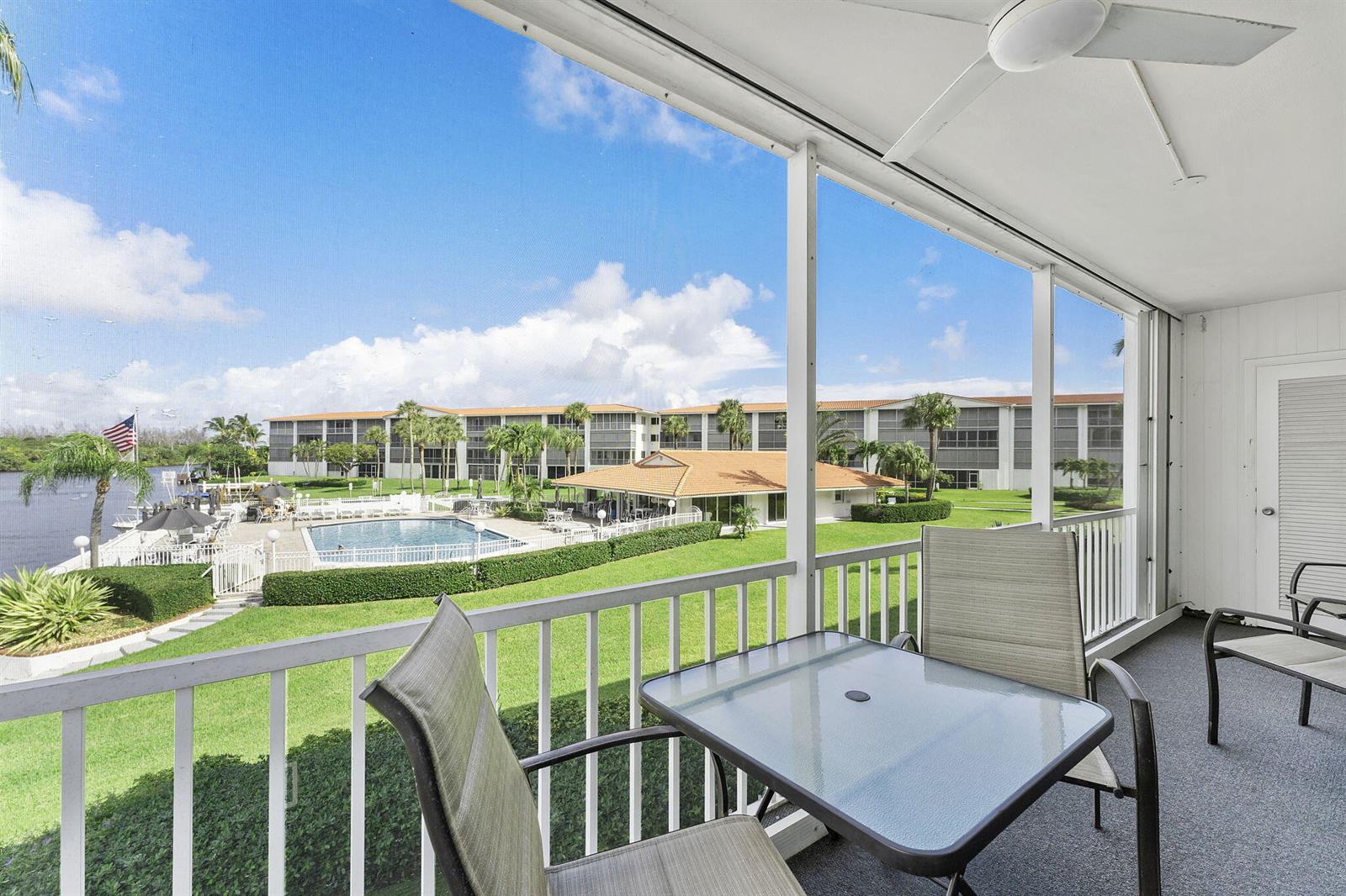 A screened-in balcony features a glass-top table and chairs overlooking a pool and lake — 101 NE 19th Avenue # 228, Deerfield Beach FL 33441, DEERFIELD BEACH, FL