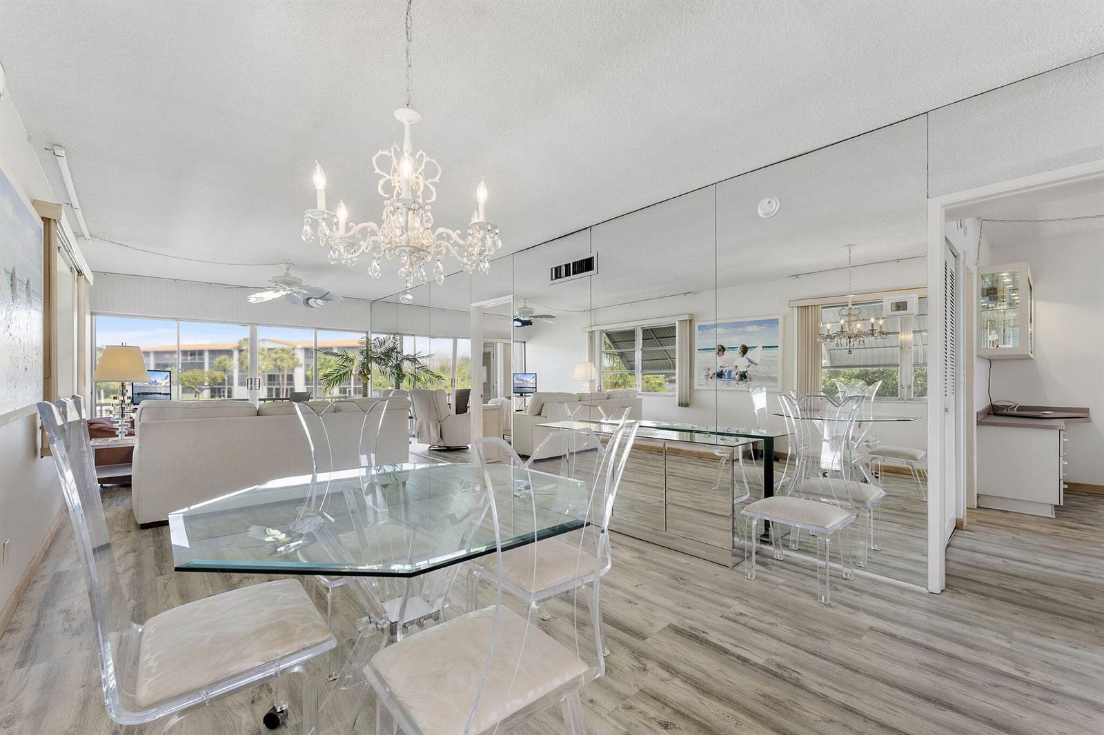 A dining area with a glass table and clear chairs sits before a mirrored wall — 101 NE 19th Avenue # 228, Deerfield Beach FL 33441, DEERFIELD BEACH, FL