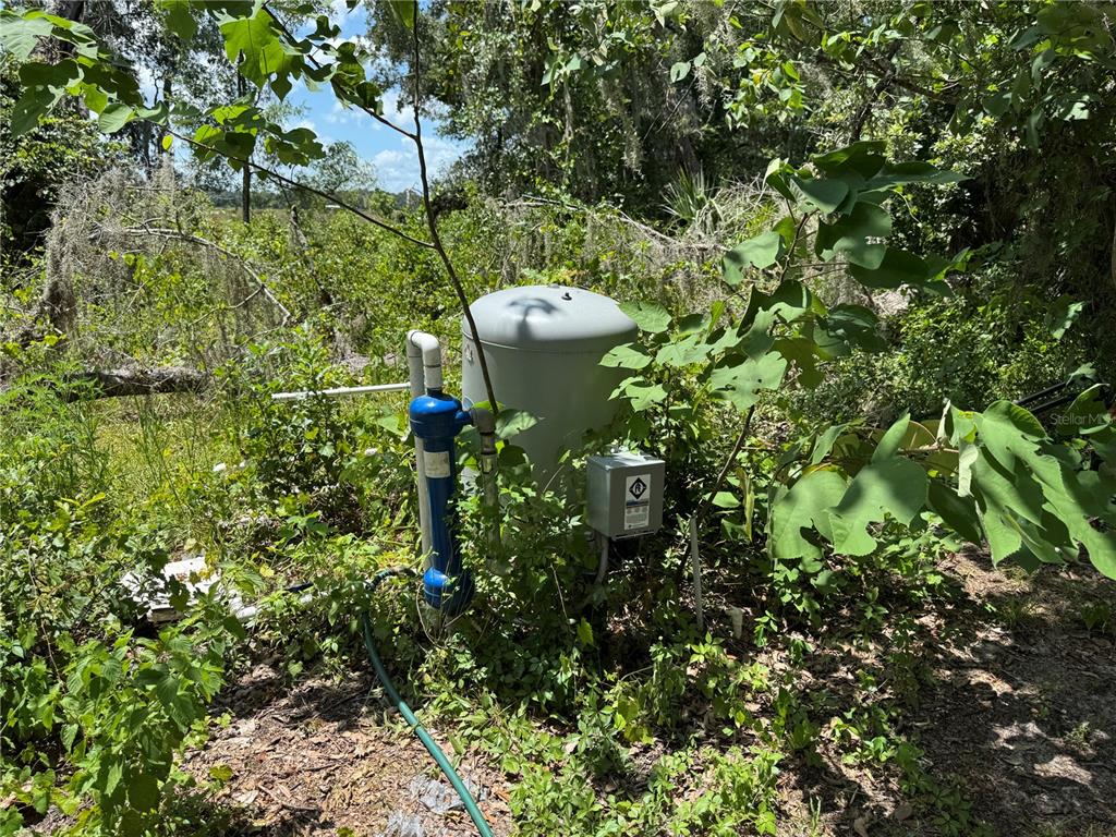 A well pump and pressure tank are situated outdoors among overgrown vegetation and trees — 1220 N US HIGHWAY 41, DUNNELLON, FL