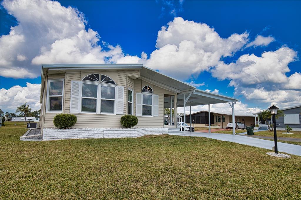A single-story manufactured home features light siding, white shutters, a carport, and a grassy lawn — 565 MADERO, NORTH PORT, FL