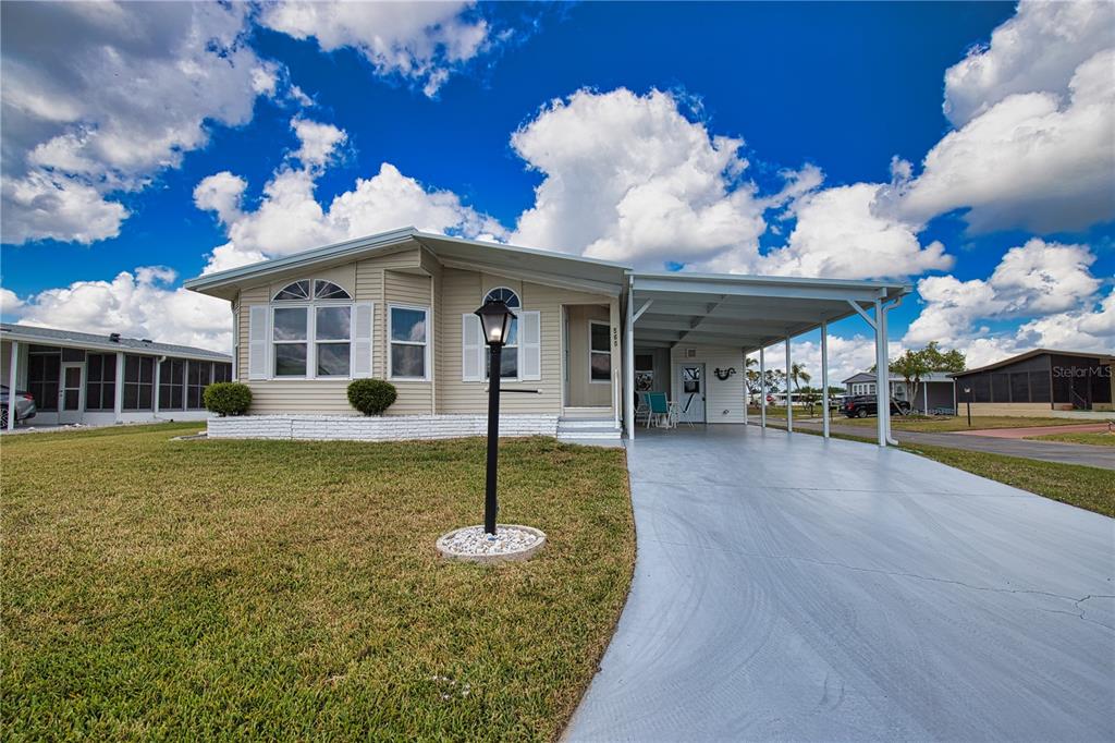 A single-story manufactured home with light siding, a carport, and a front lawn — 565 MADERO, NORTH PORT, FL
