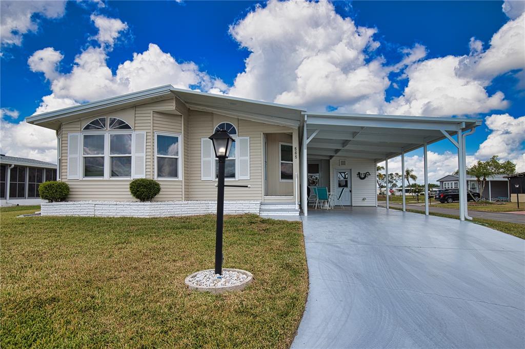 A single-story manufactured home with beige siding, a white brick base, and a covered carport — 565 MADERO, NORTH PORT, FL