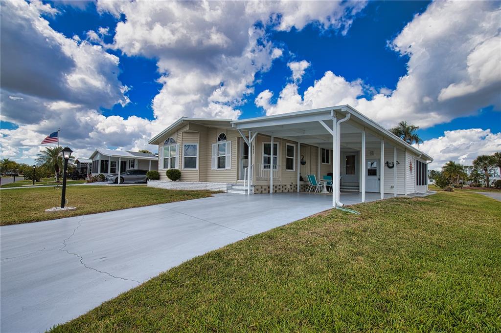 A light-colored manufactured home features a concrete driveway, a covered carport, and a grassy lawn — 565 MADERO, NORTH PORT, FL