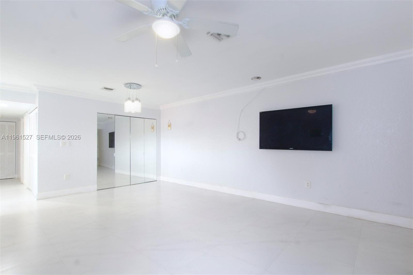 A bright, minimalist room features white tile floors, a ceiling fan, and a wall-mounted television — 49 Majorca Ave # 303, Coral Gables FL 33134, CORAL GABLES, FL