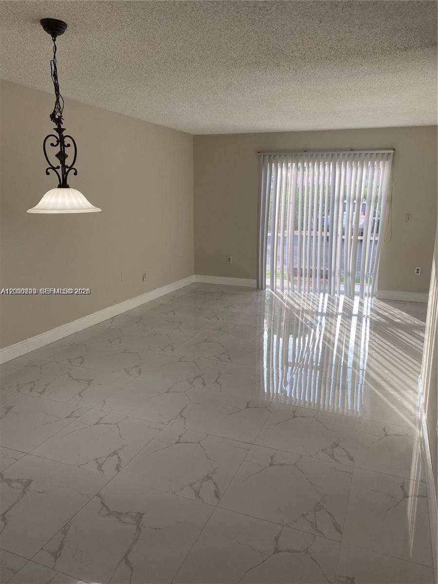 An empty dining area features white marble-look tile flooring, a hanging pendant light, and vertical blinds — 11307 SW 200th St # B, Miami FL 33157, MIAMI, FL