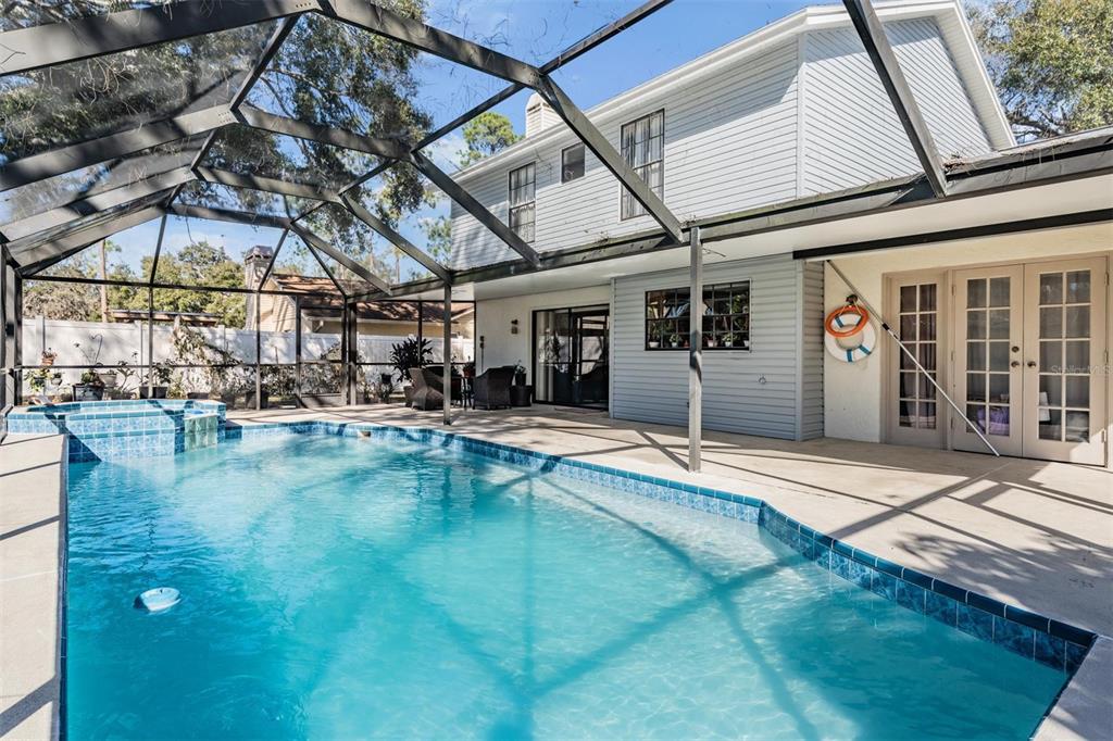 A swimming pool with a spa sits inside a screened enclosure next to a house — 12604 RAIN FOREST STREET, TEMPLE TERRACE, FL