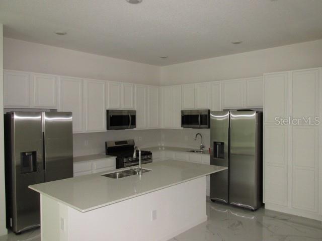A kitchen features white cabinetry, stainless steel appliances, and a large central island — 1275 BUTTERFLY ORCHID ROAD, DAVENPORT, FL