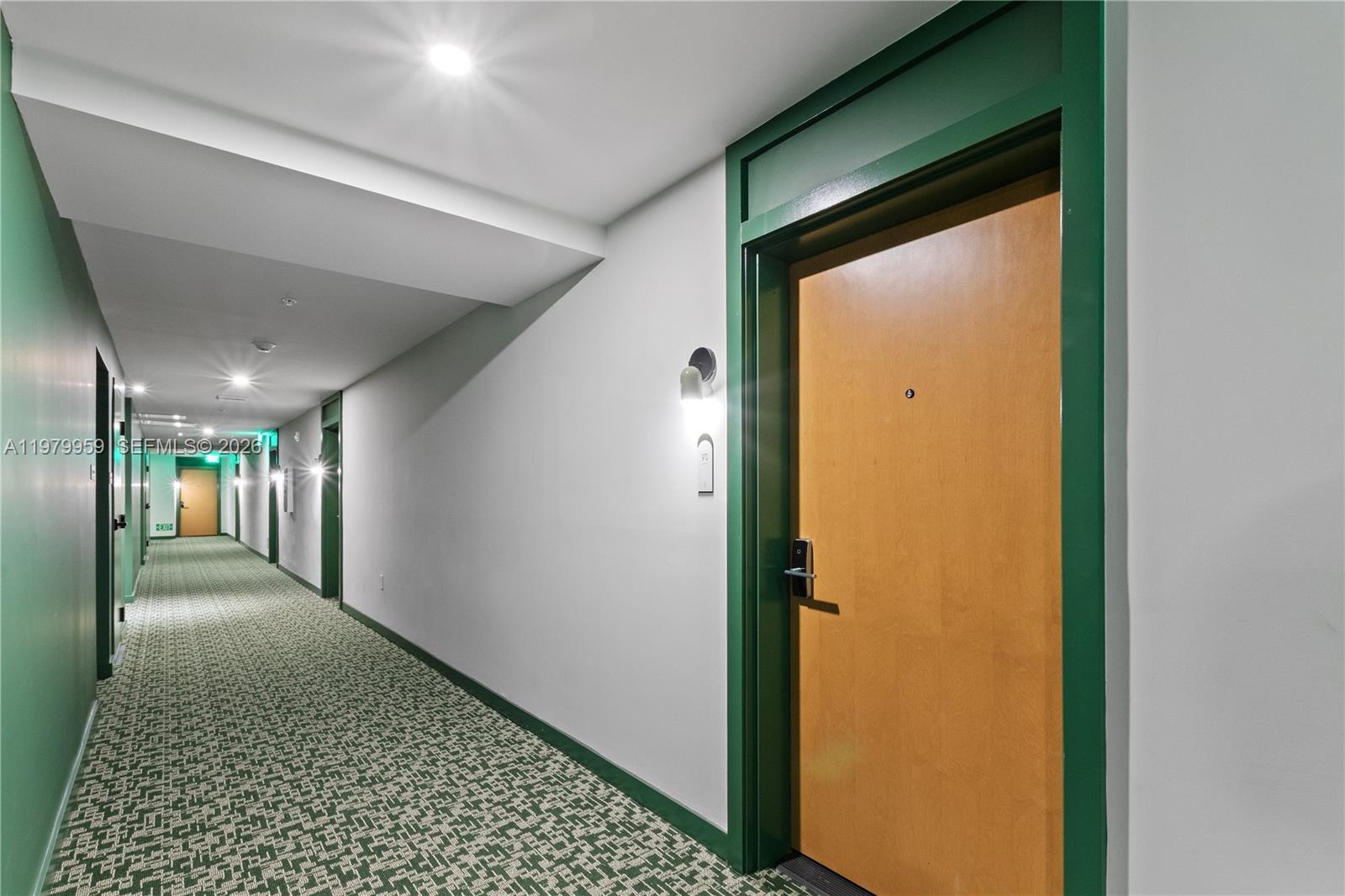 A hallway with green patterned carpet, white walls, and wooden doors with green trim — 11 NE 6 ST # 910, Miami FL 33132, MIAMI, FL