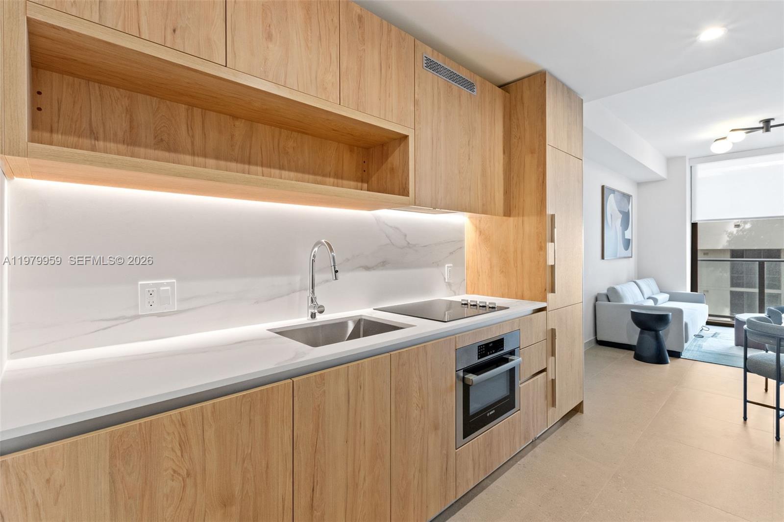 A modern kitchen features light wood cabinetry, white marble-style countertops, and integrated stainless steel appliances — 11 NE 6 ST # 910, Miami FL 33132, MIAMI, FL
