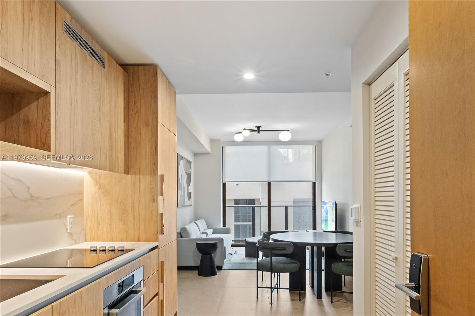 A modern kitchen with light wood cabinetry opens into a living and dining area — 11 NE 6 ST # 910, Miami FL 33132, MIAMI, FL
