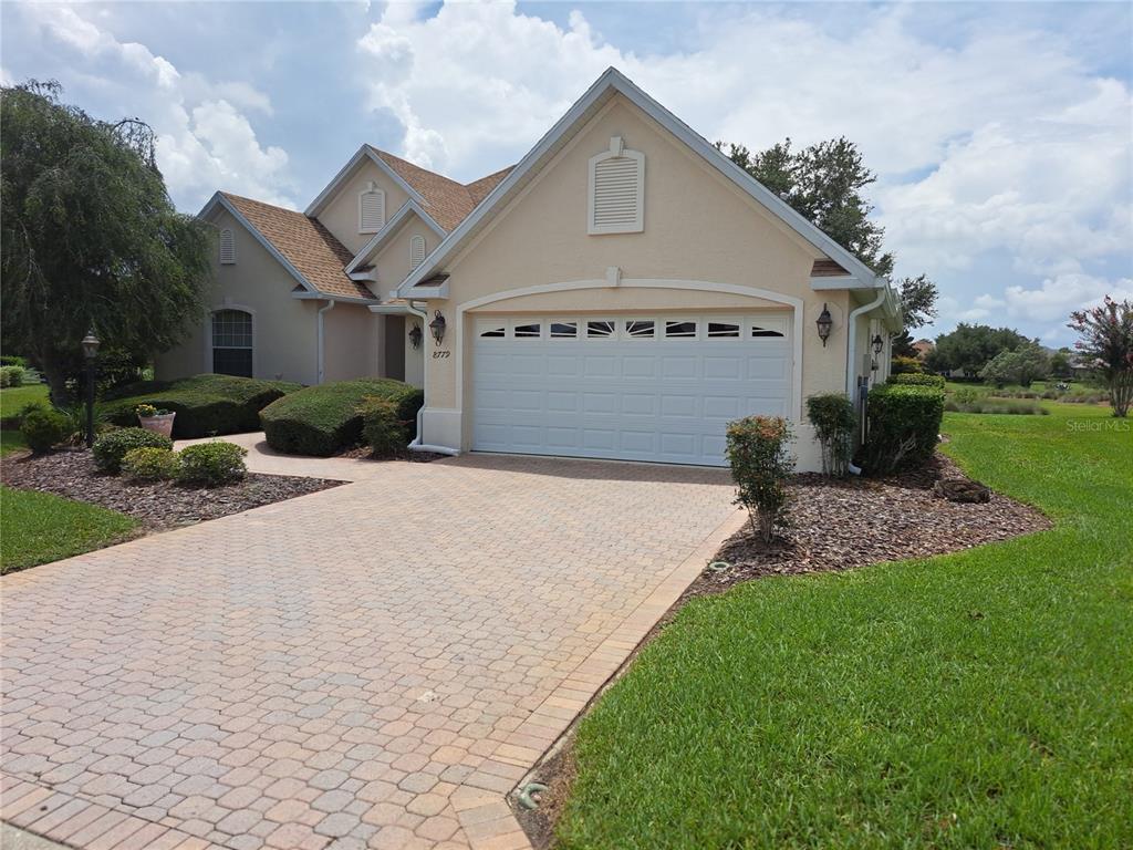 A beige house with a two-car garage and a paved driveway under a cloudy sky — 8779 SW 83RD CIRCLE, OCALA, FL