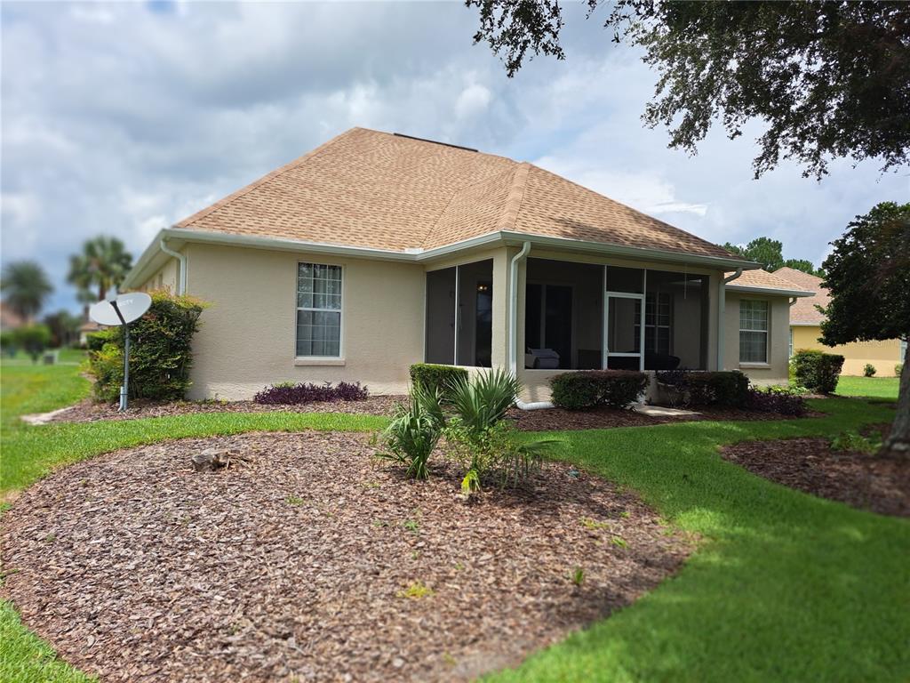 The rear exterior of a tan house features a screened-in porch and a landscaped yard — 8779 SW 83RD CIRCLE, OCALA, FL