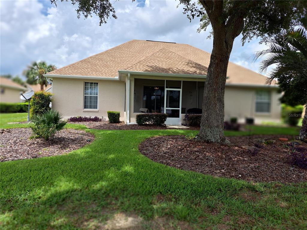 The rear exterior of a beige house features a screened-in lanai and a large tree — 8779 SW 83RD CIRCLE, OCALA, FL