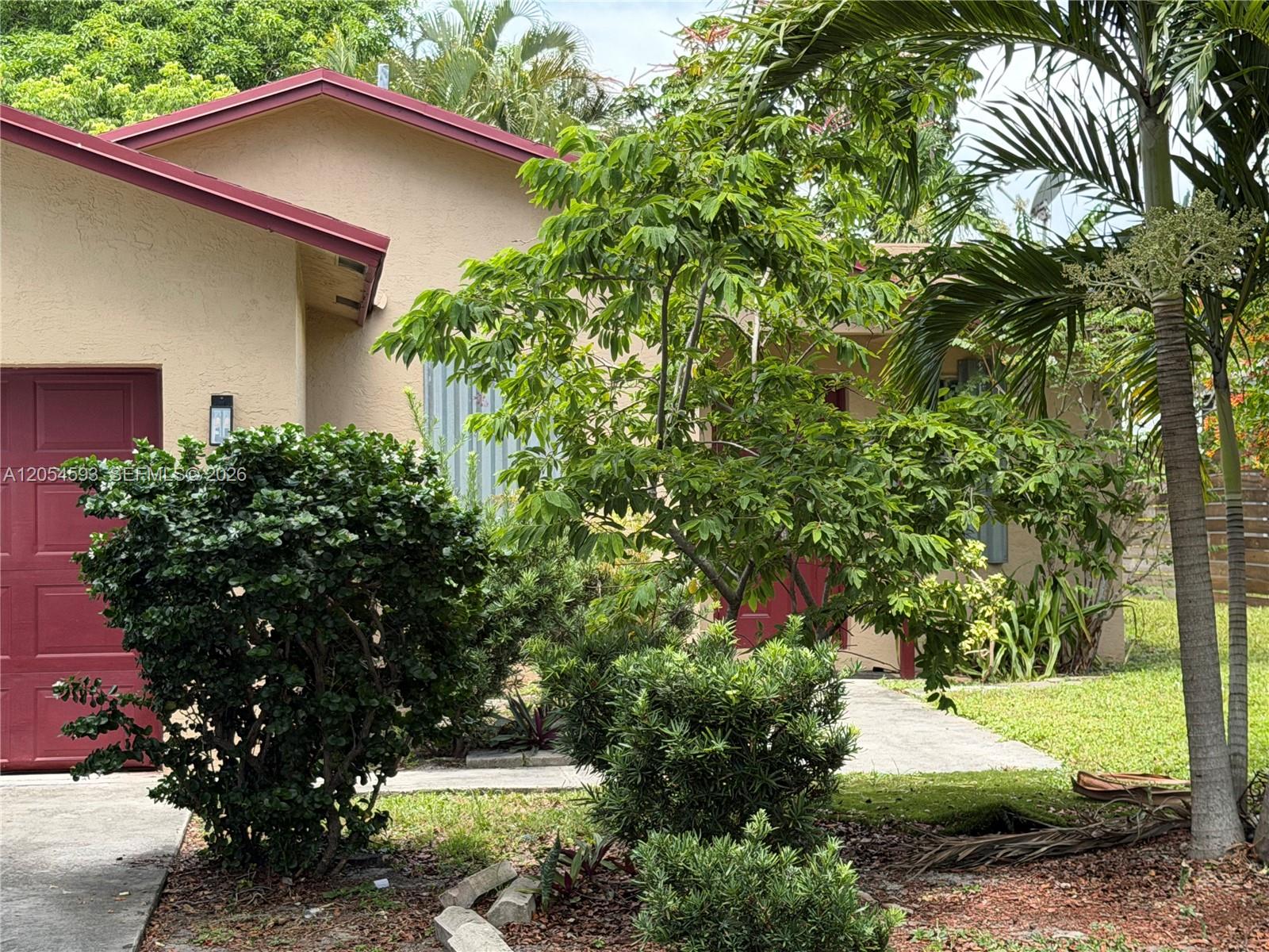 A tan house with a red garage door and roof trim is surrounded by landscaping — 1561 NW 7th Ter, Pompano Beach FL 33060, POMPANO BEACH, FL