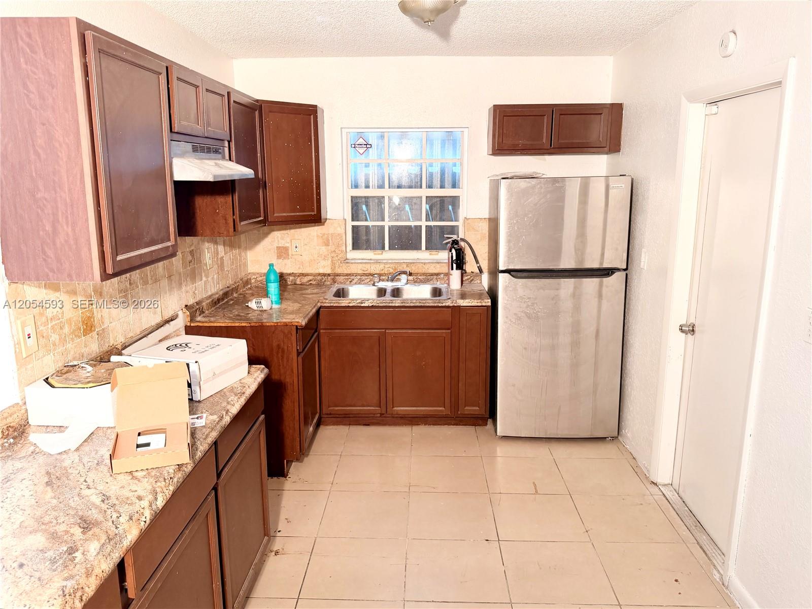 A kitchen features dark wood cabinets, stainless steel appliances, tile flooring, and a window — 1561 NW 7th Ter, Pompano Beach FL 33060, POMPANO BEACH, FL