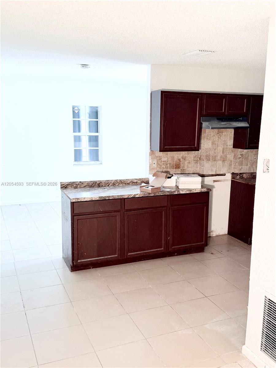 A kitchen features dark wood cabinets, a laminate countertop, and light-colored tile flooring — 1561 NW 7th Ter, Pompano Beach FL 33060, POMPANO BEACH, FL