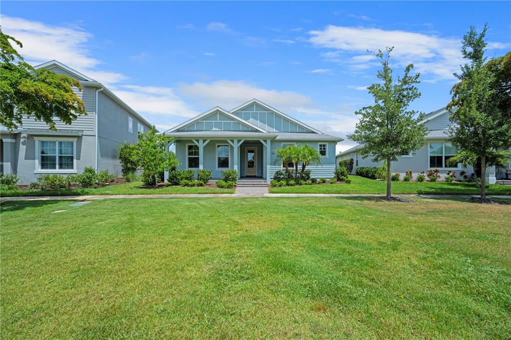 A light blue, single-story house with a front porch sits behind a large grassy lawn — 17057 PINE LILY LANE, PUNTA GORDA, FL