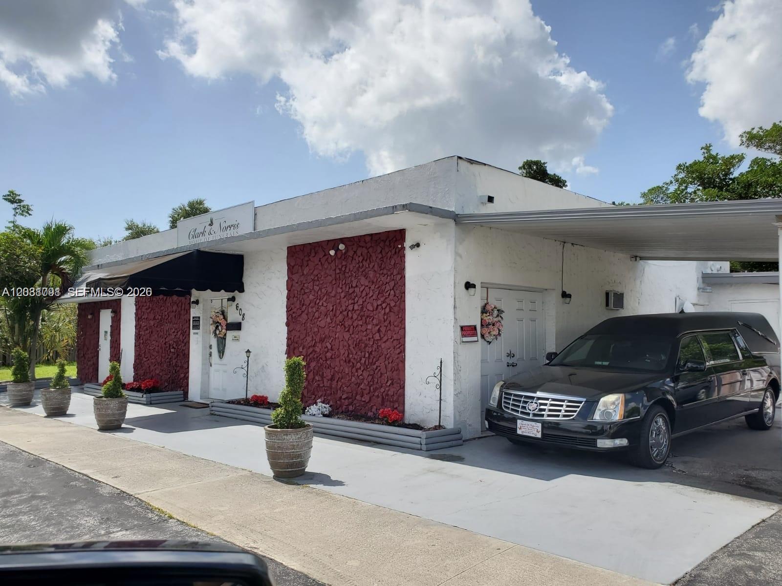 A single-story funeral home building features white walls, red stone accents, and a black hearse — 608 SW 12th Ave, Dania Beach FL 33004, DANIA BEACH, FL