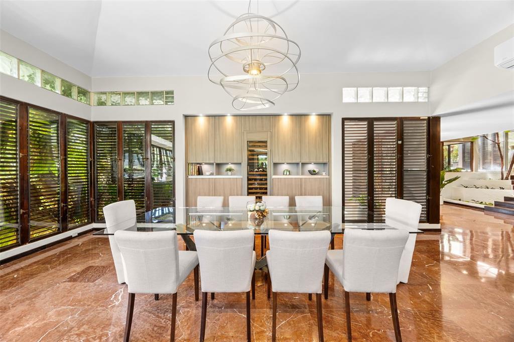 A dining room features a glass table, white chairs, marble floors, and a modern chandelier — H A 28  VILLA CAPARRA, GUAYNABO, PR