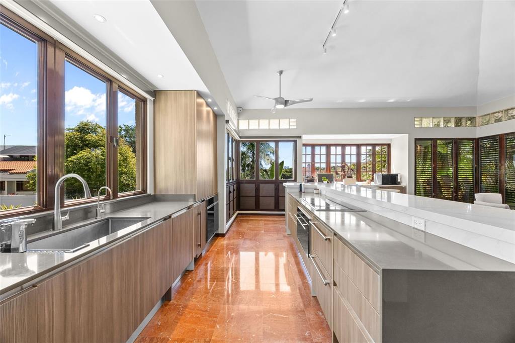 A modern kitchen features wood-grain cabinetry, a long white island, and orange marble flooring — H A 28  VILLA CAPARRA, GUAYNABO, PR