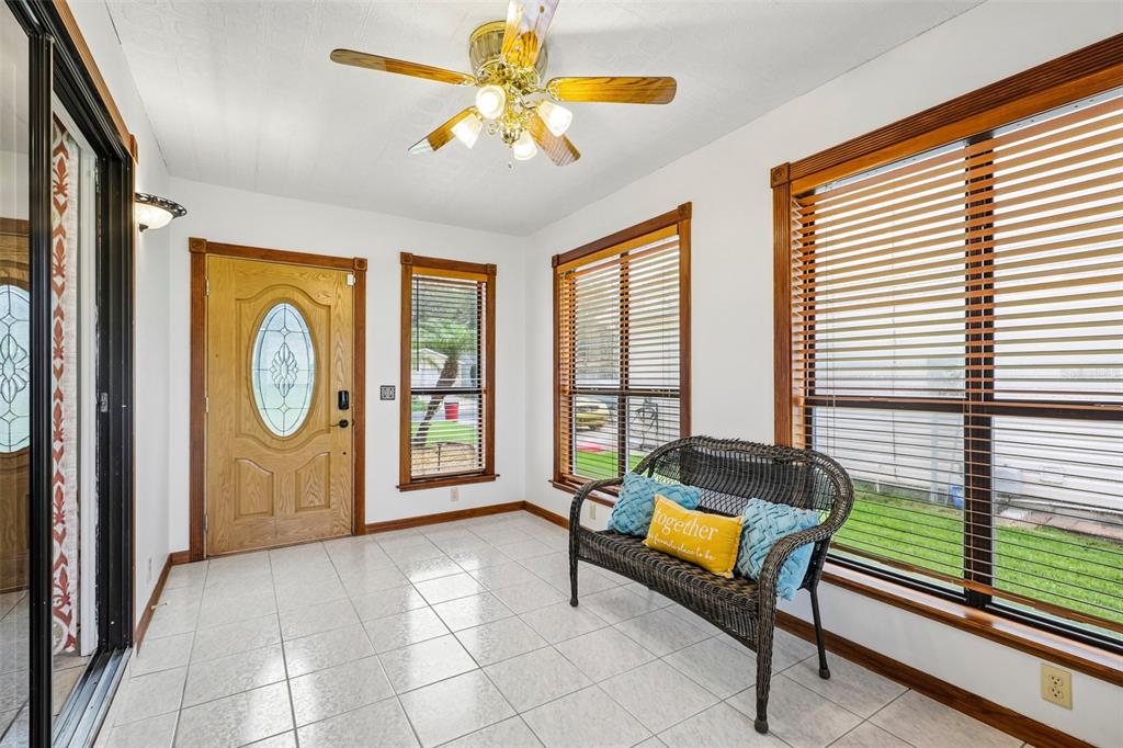 A sunroom features white tile floors, a ceiling fan, and a wicker bench by windows — 710 CORTEZ AVENUE, THE VILLAGES, FL