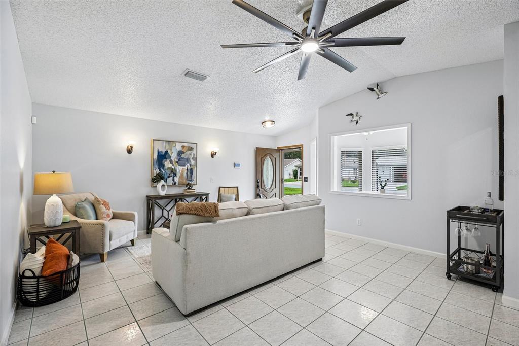 A living room with light tile floors, a beige sofa, an armchair, and a ceiling fan — 710 CORTEZ AVENUE, THE VILLAGES, FL