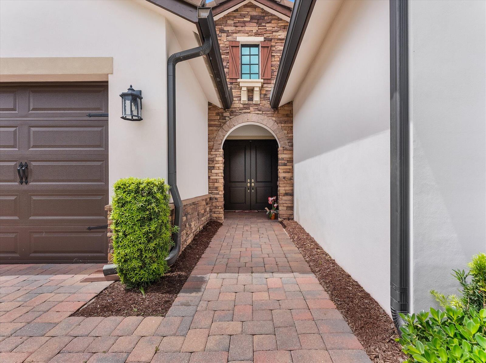 A paved walkway leads to a dark double-door entrance framed by stone and stucco walls — 8259 Grand Prix Lane, Boynton Beach FL 33472, BOYNTON BEACH, FL