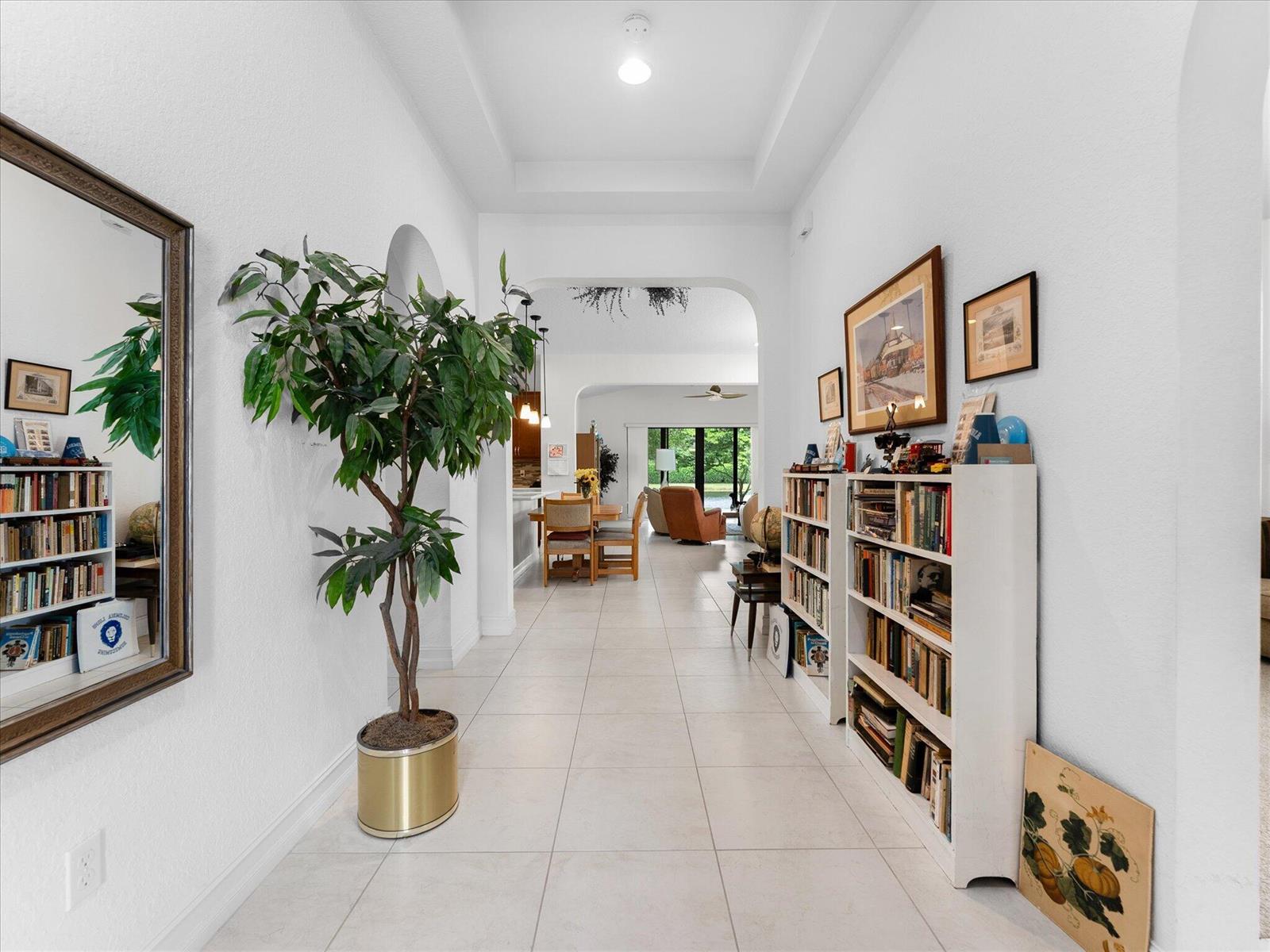 A tiled hallway features a large potted plant, white bookshelves, and an arched entryway — 8259 Grand Prix Lane, Boynton Beach FL 33472, BOYNTON BEACH, FL